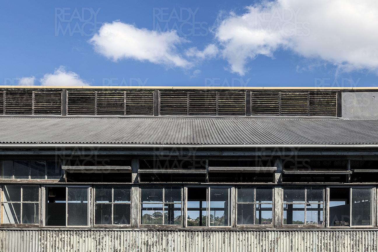 Architectural photo of a building facade in the Ship Deign Precinct at Cockatoo Island, Sydney, Australia showing rusted metal sheet cladding and glass windows with roof ventilation louvres