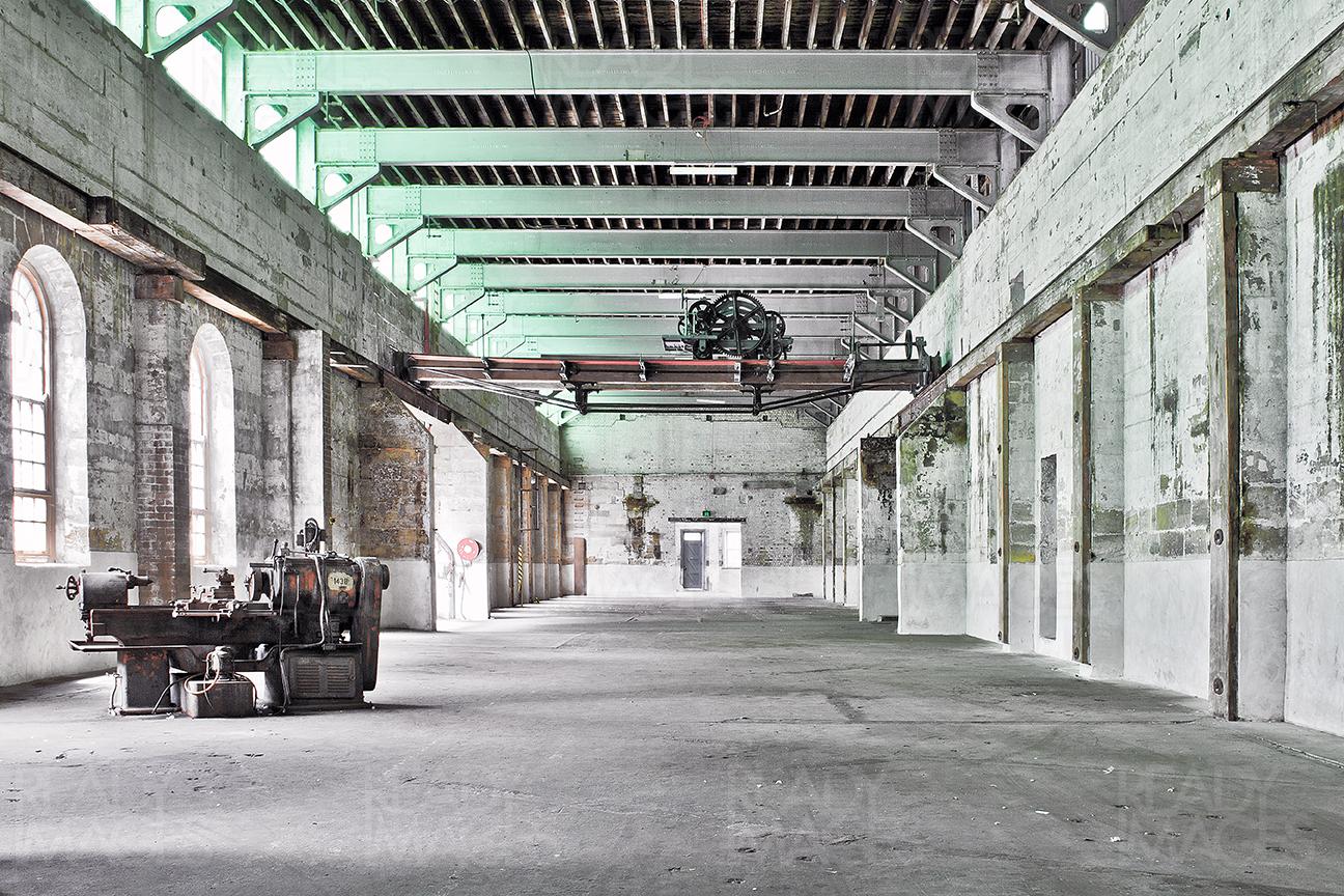 One point perspective of a building in the Industrial Design Precinct showing abandoned space surrounded by concrete walls and steel structure with an old machine inside at Cockatoo Island, Sydney, Australia