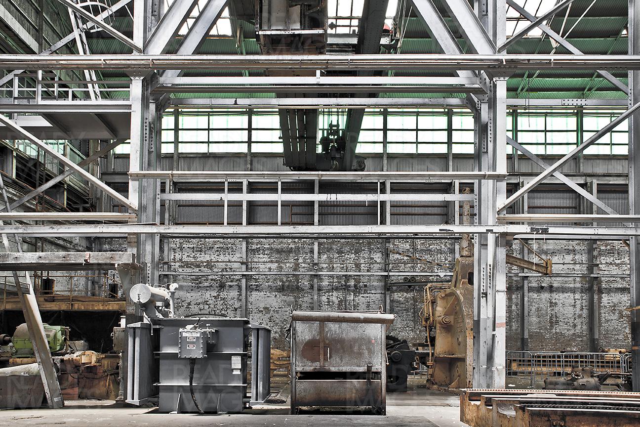 Grey concrete walls, steel structure and an old machine in a building of the Industrial Design Precinct showing abandoned space at Cockatoo Island, Sydney, Australia