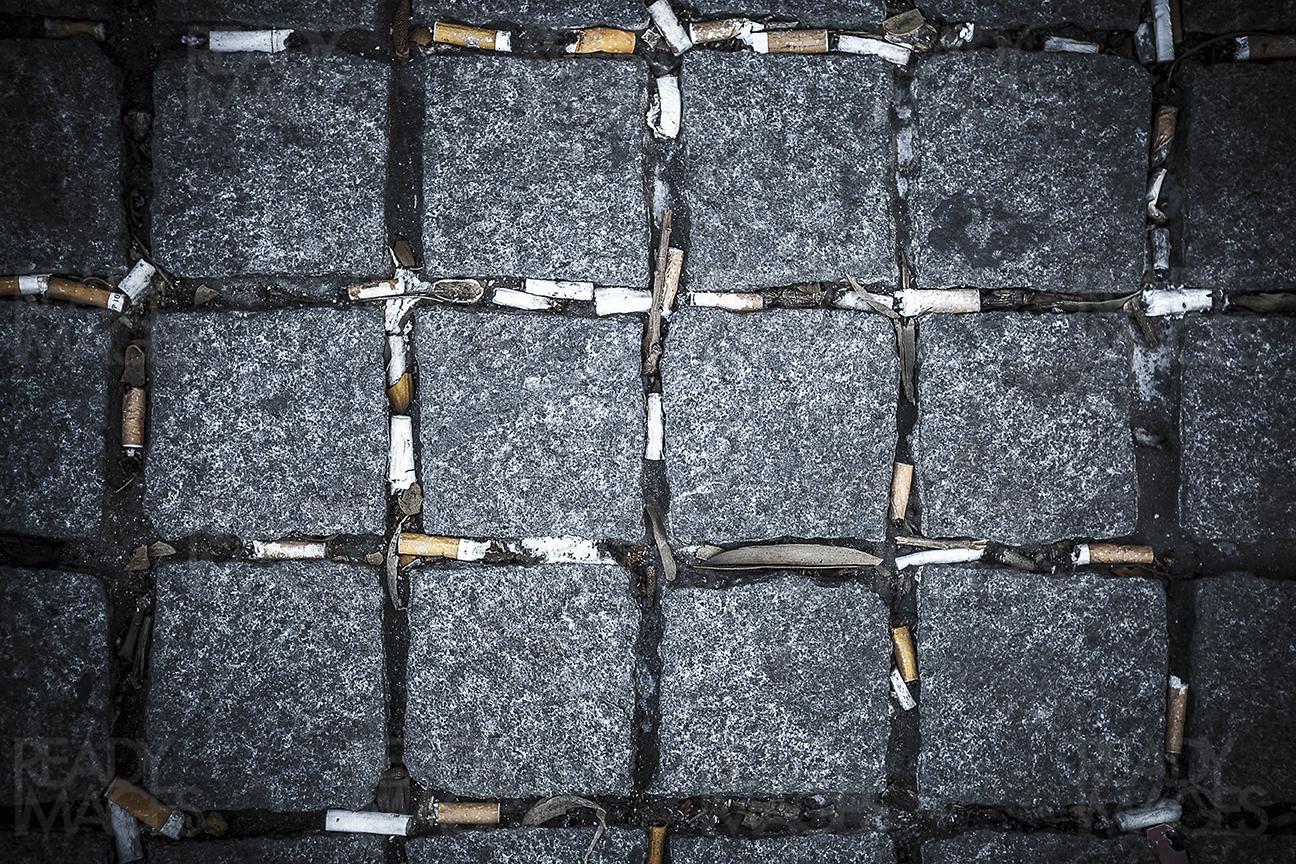 Abstract view from above of a cobbled grey square stone pavement tiles with cigarette butts litter on a pedestrian street of Sydney CBD