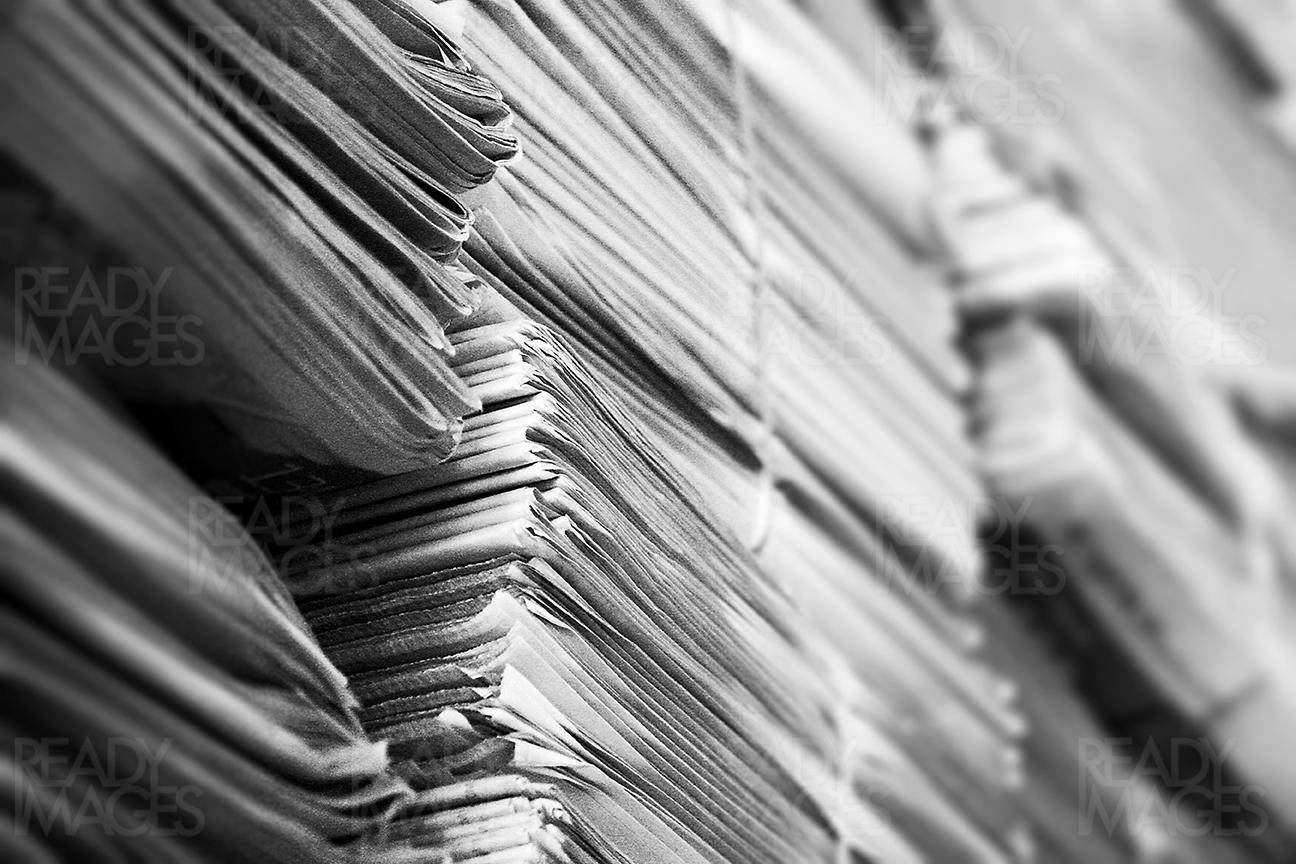 Black and white abstract image of a large pile of old newspapers stacked and arranged in an order