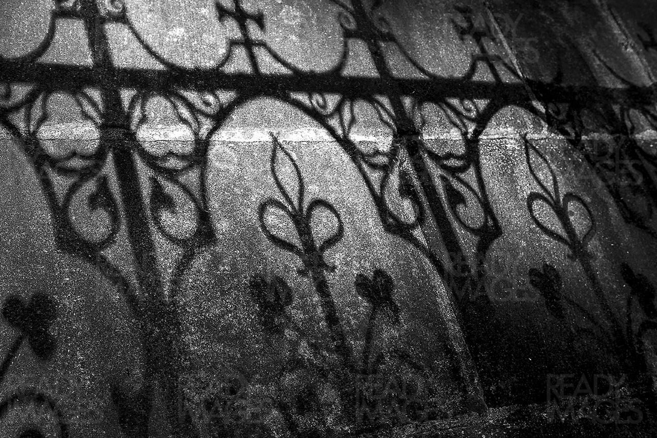 Black and white abstract image of the interesting shadow casted by ornamental railing on a stone wall