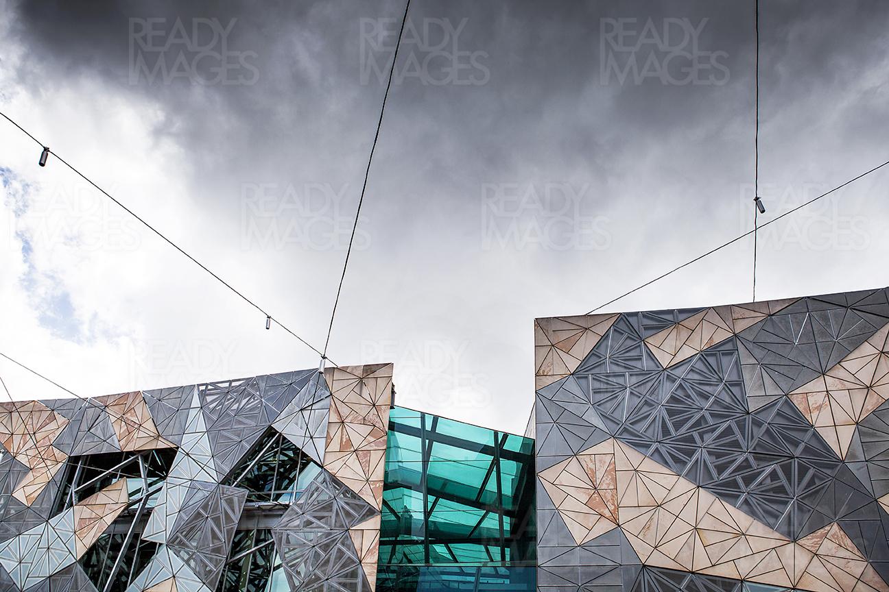 The perfect example of deconstructivist style architecture, Federation Square building facades are cladded with zinc, glass, sandstone, using pinwheel tiling, This picture is taken on an overcast day with dramatic dark clouds forming on top of the image