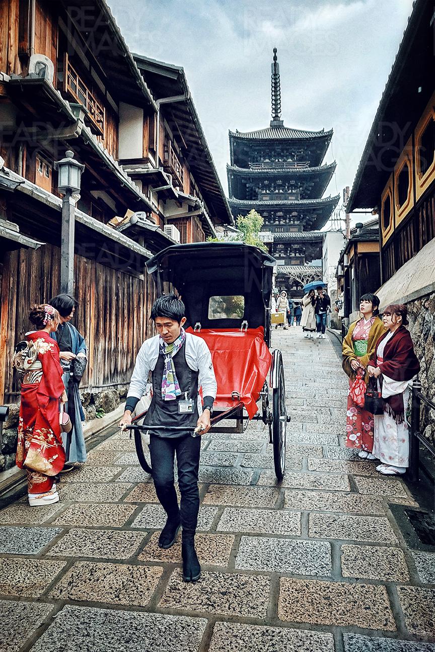 Image of onlooking tourists in traditional kimonos and private tour rickshaw passing through the geisha/ Higashiyama district of Gion with Yasaka Pagoda (Hokanji Temple) in the background